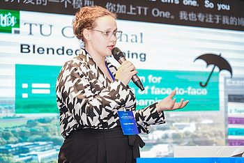 Frau in Konferenzkleidung mit Mikrofon im Hintergrund Powerpointfolie mit den Worten Blended Learning 
